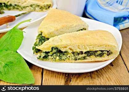 Two pieces of pie with spinach and cheese on a plate, spinach leaves, cup, knife, napkin on wooden board