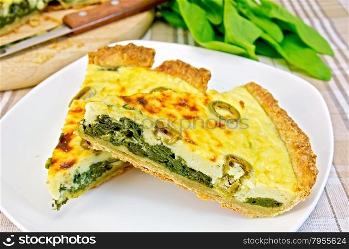 Two pieces of pie with spinach, cheese and olives on a plate, spinach leaves, knife on the background of a linen tablecloth