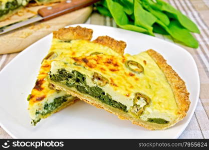 Two pieces of pie with spinach, cheese and olives on a plate, spinach leaves, knife on the background of a linen tablecloth