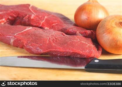 Two pieces of raw steak, a chef&acute;s knife and a couple of onions, a good start for many different dishes