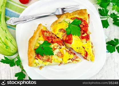 Two pieces pie of zucchini with tomatoes and eggs in a plate on a napkin, parsley on a background of wooden boards on top