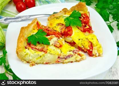 Two pieces pie of zucchini with tomatoes and eggs in a white plate on a napkin, parsley on the background light wooden boards