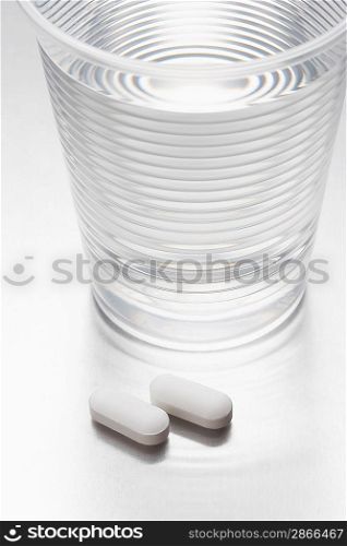 Two pills beside water in plastic cup
