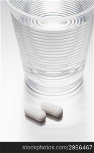 Two pills beside water in plastic cup