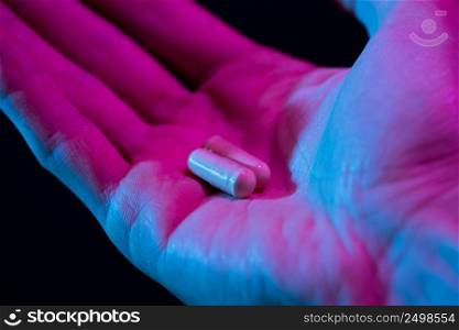 Two pills in hand closeup on dark background. Drugs tablet in palm.