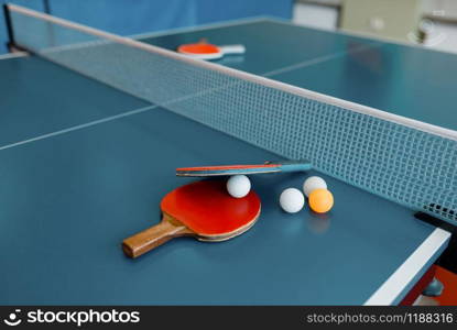 Two ping pong rackets and balls on game table with net, nobody, closeup view. Table-tennis club, tennis concept, ping-pong. Ping pong rackets and balls on game table with net
