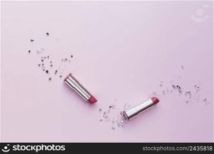 two pink lipsticks with crushed glass pieces pink background