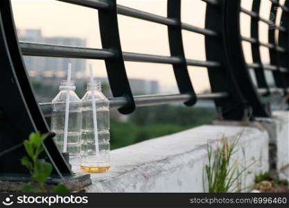 Two plastic bottle with straw leave on bridge railing on urban street at Ho Chi Minh city, Vietnam, bad habit make environmental pollution, low angle with blurred background