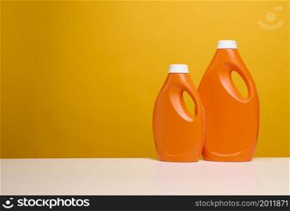 two plastic orange bottles with liquid detergent stand on a white table, yellow background
