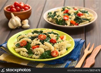 Two plates of fusilli pasta with chard leaves (lat. Beta vulgaris) and cherry tomatoes, photographed on dark wood with natural light (Selective Focus, Focus in the middle of the first dish)