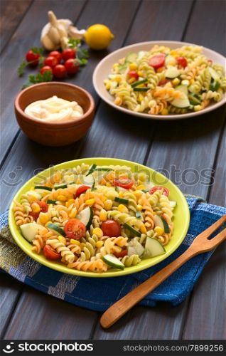 Two plates of vegetarian pasta salad made of tricolor fusilli, sweet corn, cucumber and cherry tomato with mayonnaise in the back, photographed with natural light (Selective Focus, Focus one third into the first salad)