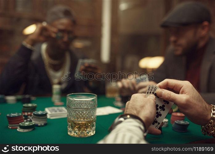 Two poker players with cards sitting at gaming table with green cloth in casino. Games of chance addiction, risk, gambling house. Men leisures with whiskey and cigars. Two poker players with cards in casino