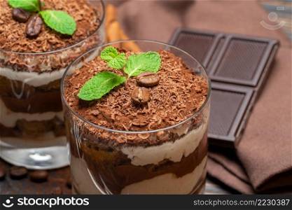 two portions Classic tiramisu dessert in a glass and chocolate bar on wooden background or table. two portions Classic tiramisu dessert in a glass and chocolate bar on wooden background