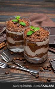 two portions Classic tiramisu dessert in a glass and chocolate bar on wooden background or table. two portions Classic tiramisu dessert in a glass and chocolate bar on wooden background