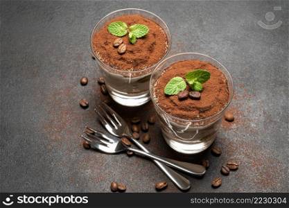 two portions Classic tiramisu dessert in a glass on dark concrete background or table. two portions Classic tiramisu dessert in a glass on dark concrete background