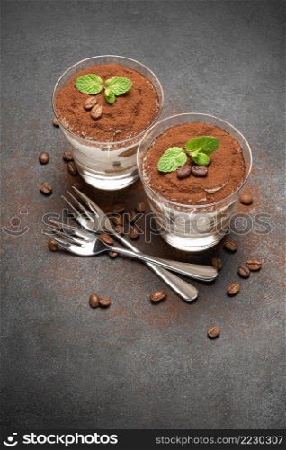 two portions Classic tiramisu dessert in a glass on dark concrete background or table. two portions Classic tiramisu dessert in a glass on dark concrete background