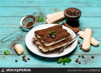 Two portions of Classic tiramisu dessert on ceramic plate and savoiardi cookies on colorful blue wooden background or table. Two portions of Classic tiramisu dessert on ceramic plate and savoiardi cookies on colorful blue wooden background