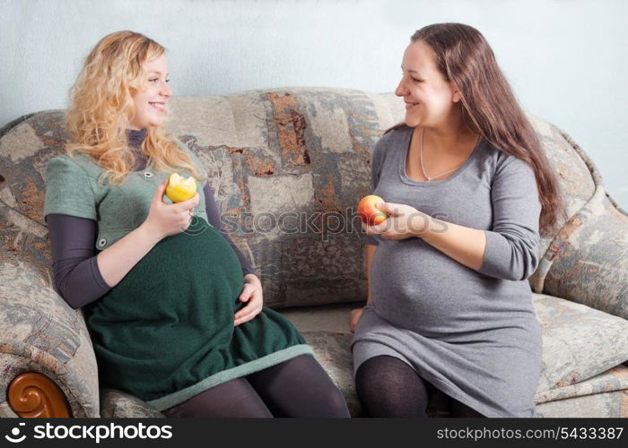 Two pregnant women eat fruits and discuss pregnancy