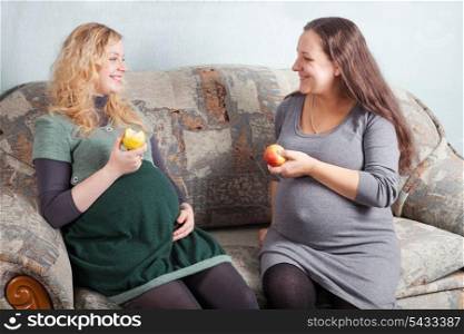 Two pregnant women eat fruits and discuss pregnancy