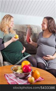 Two pregnant women eat fruits and discuss pregnancy and preparation to parenting