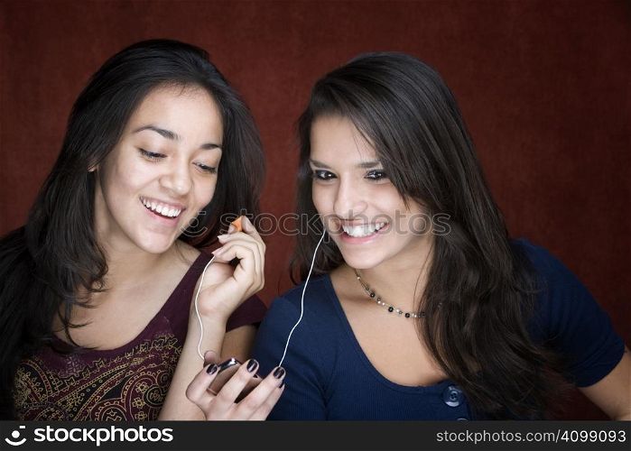 Two pretty Hispanic women sharing a headset listening to music