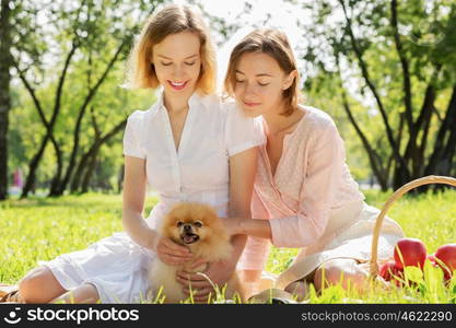 Two pretty ladies in park with their cute pet. In park with loving pet