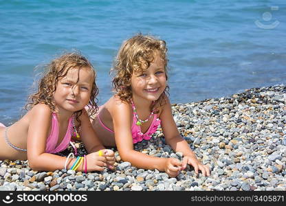 two pretty little girls lying on stony beach near sea