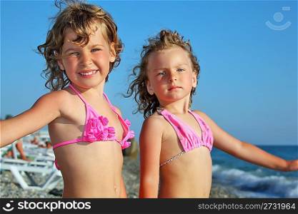 two pretty little girls on beach near sea, placed hands in sides