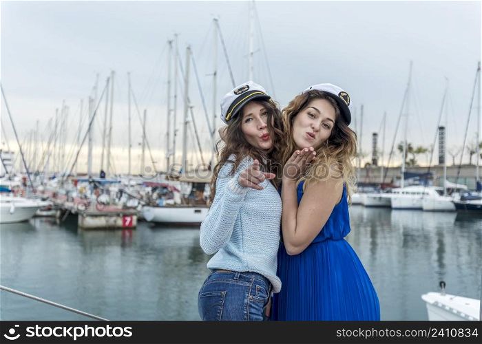 Two pretty model women standing and posing on a sailboat while kissing to camera