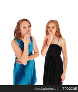 Two pretty teen girls in blue and black dresses standing with there handsover there mouth, isolated for white background.