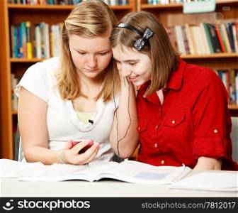 Two pretty teen girls in the school library, listening to an mp3 player.