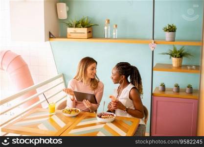Two pretty young black and caucasian woman having good time, drinking fresh juices and having healthy breakfast in the cafe