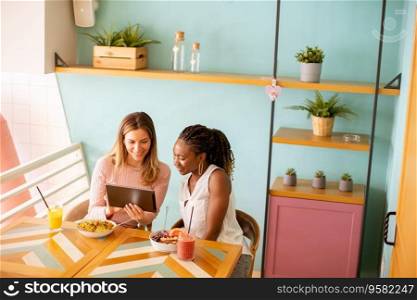 Two pretty young black and caucasian woman having good time, drinking fresh juices and having hea<hy breakfast in the cafe