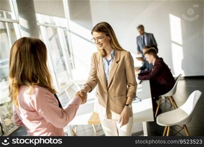 Two pretty young business women giving friendly handshake in the office
