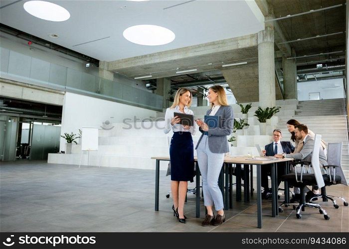 Two pretty young business women looking at financial results on digital tablet in front of their team at the office