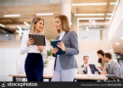 Two pretty young business women looking at financial results on digital tablet in front of their team at the office