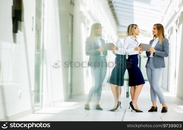 Two pretty young business women with digital tablet in the office hallway