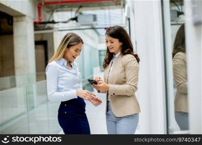 Two pretty young business women with mobile phone in the office hallway