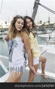 Two pretty young women back to back on a catamaran on harbor.