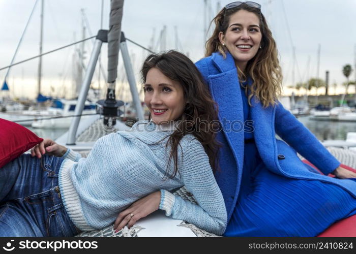 Two pretty young women back to back on a catamaran on harbor.