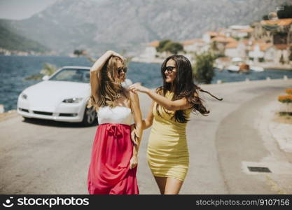 Two pretty young women by white cabriolet car on the seaside