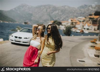 Two pretty young women by white cabriolet car on the seaside
