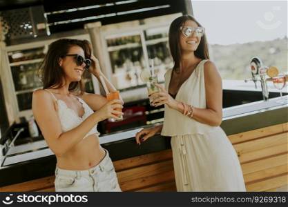 Two pretty young women  drinking coctails and having fun by the pool at hot summer day