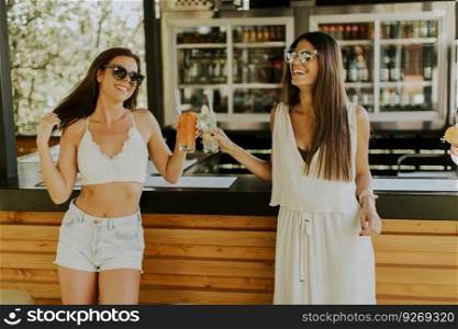 Two pretty young women  drinking coctails and having fun by the pool at hot summer day