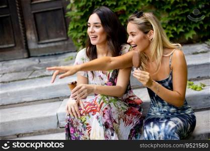 Two pretty young women sitting and eating ice cream by the old house with ivy