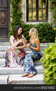 Two pretty young women sitting and eating ice cream by the old house with ivy