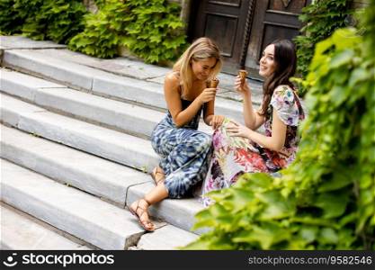 Two pretty young women sitting and eating ice cream by the old house with ivy