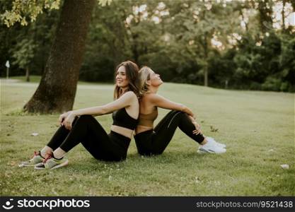 Two pretty young women sitting on the grass and relaxing after outdoor training