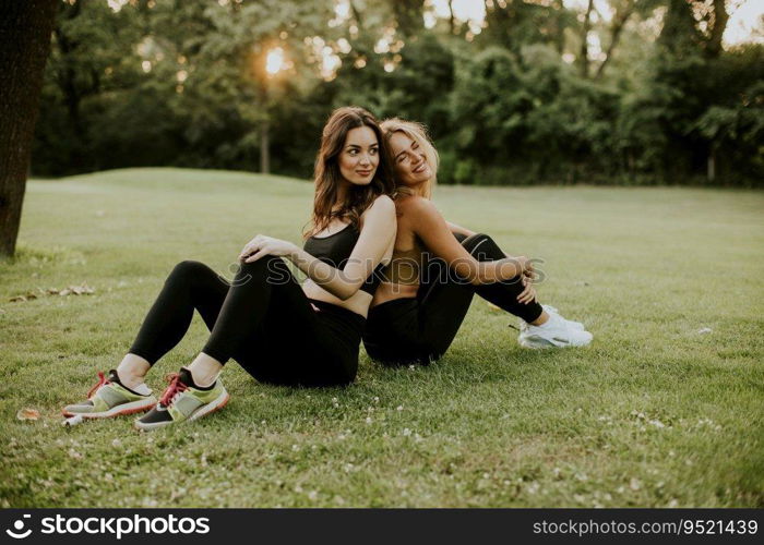 Two pretty young women sitting on the grass and relaxing after outdoor training