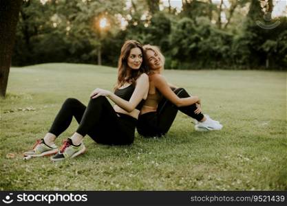 Two pretty young women sitting on the grass and relaxing after outdoor training